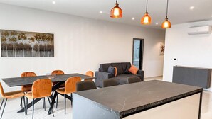 A modern living room with a dining area, featuring a marble island, orange chairs, a grey sofa, and pendant lighting. - This apartment is a 2 bedroom(s), 2 bathrooms, located in Il-Mellieħa, null. (Il-Mellieħa)