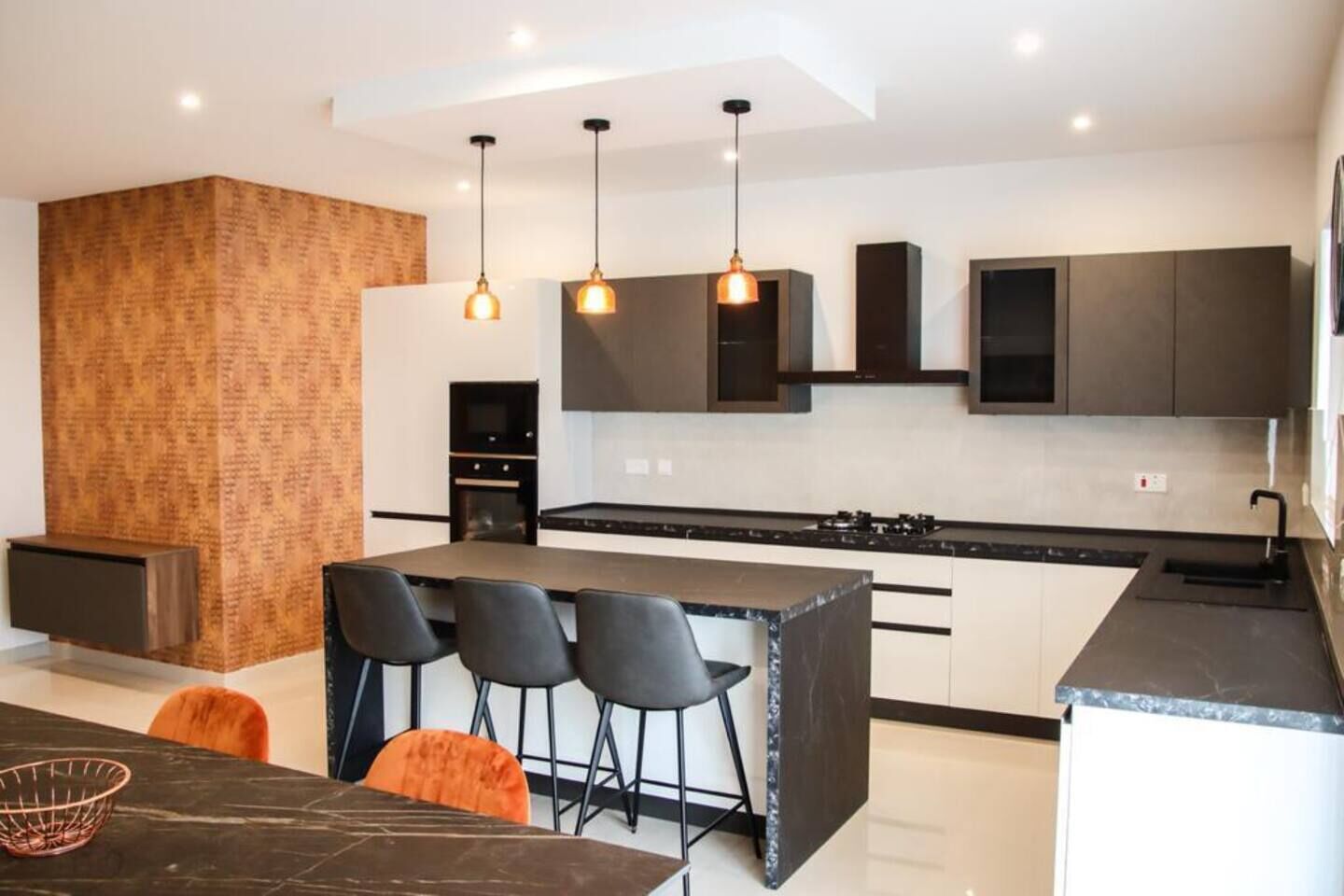 Una cocina moderna con una isla central, luces colgantes y un papel tapiz estampado.