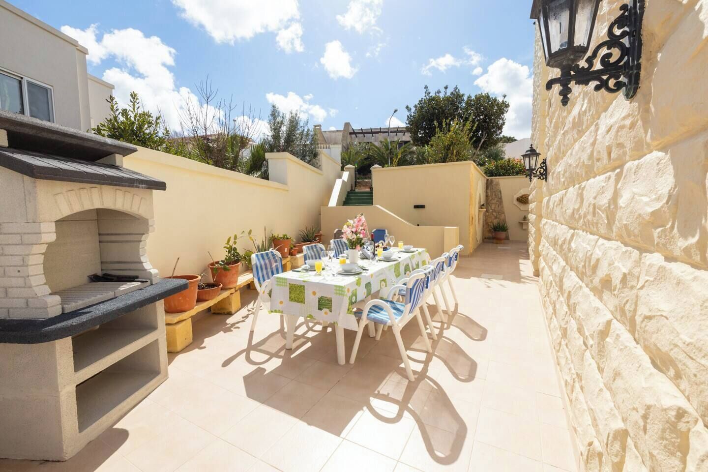 An outdoor patio with a dining table set for four, surrounded by potted plants and a stone wall.