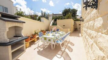 An outdoor patio with a dining table set for four, surrounded by potted plants and a stone wall.