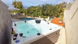 Ein Whirlpool mit Pool im Hintergrund, umgeben von viel Grün und einem Ziegeldach.