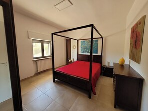A four-poster bed with a red bedspread in a room with a window, a painting on the wall, and a small table with a yellow object on it. - "Nuova Villa Ulivo" among olive and almond trees with private swimming pool (Carovigno)