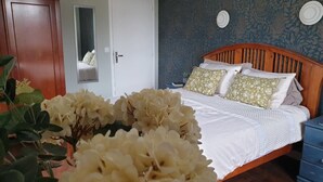 Une chambre à coucher avec un lit en bois, du linge de lit blanc et un mur orné d’un motif bleu.
