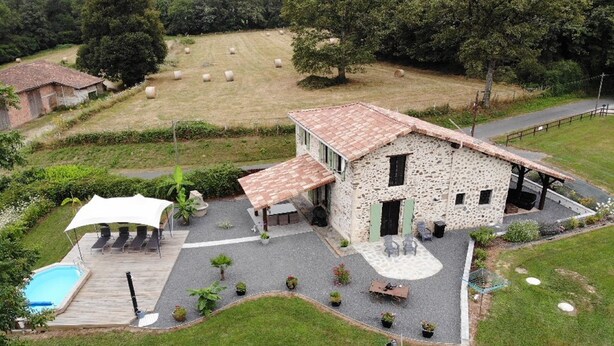 Une maison en pierre avec une piscine, un espace salon extérieur et des bottes de foin en arrière-plan.