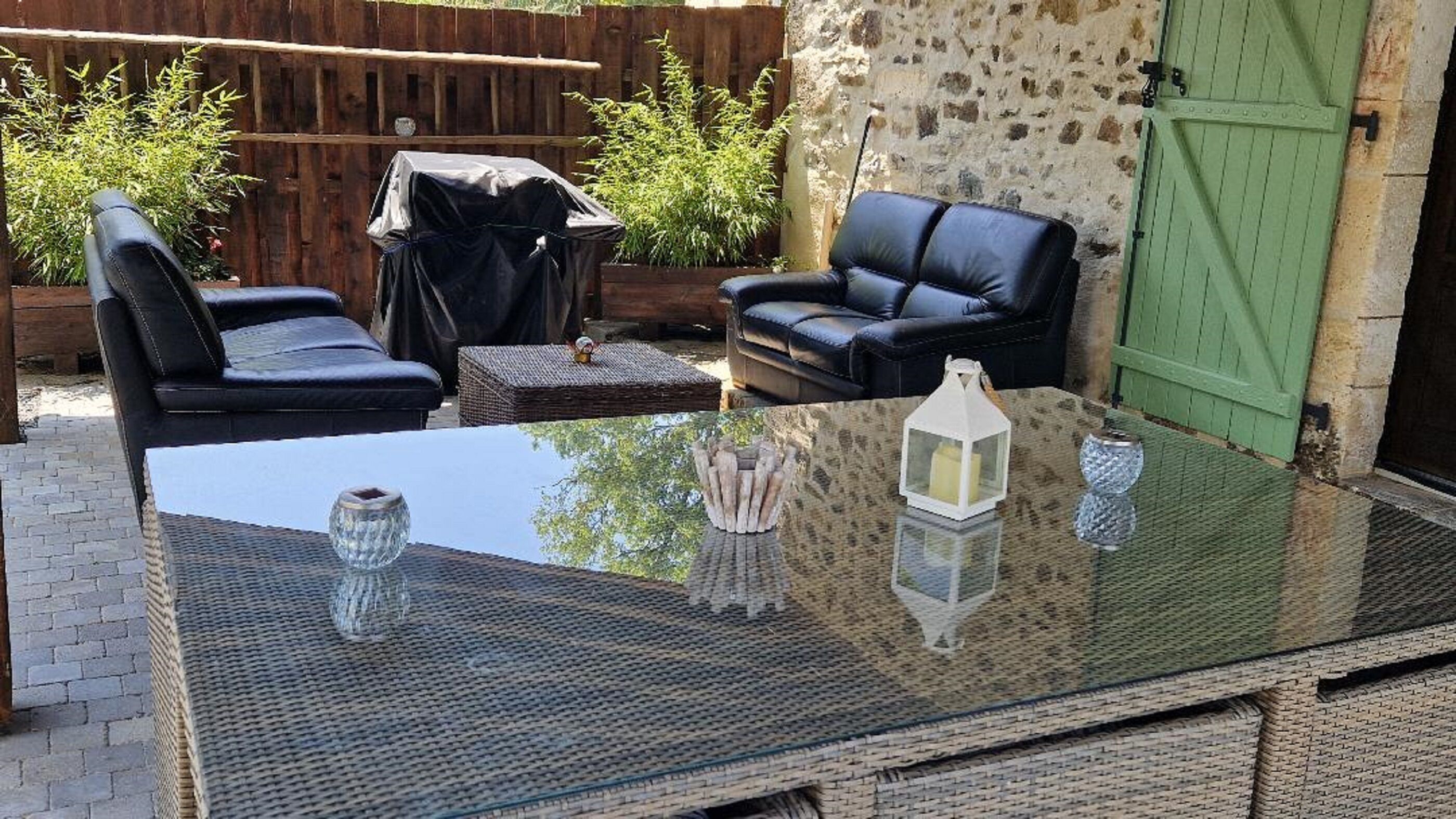 An outdoor seating area with a glass-top table, two black leather sofas, and a wicker ottoman.