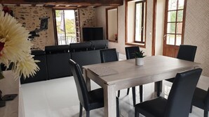 Un coin repas avec une table en bois et des chaises noires, un mur en pierre et une grande fenêtre.