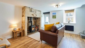 A cozy living room with a stone fireplace, a leather sofa, and a wooden floor. - Host & Stay | Rose Cottage (Thropton)