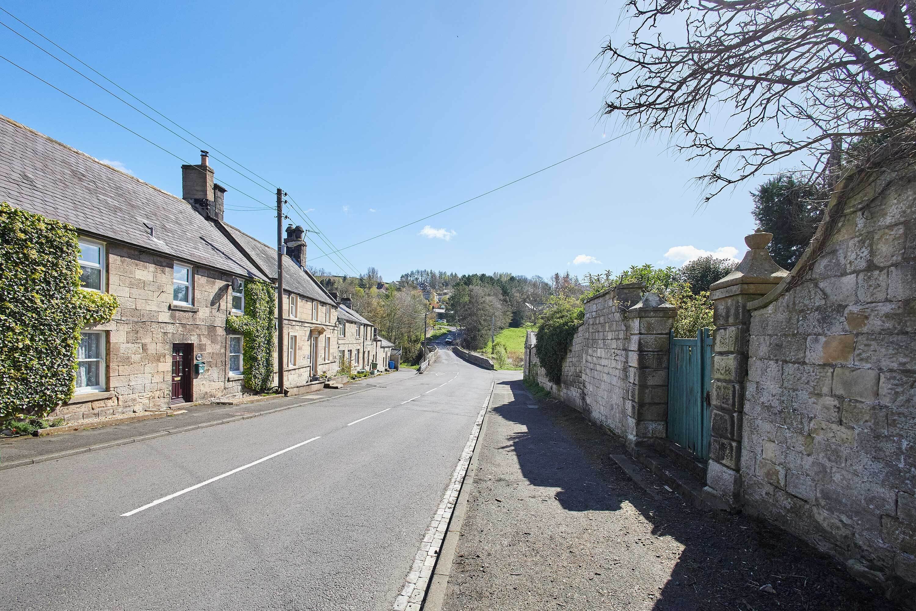 A quiet street with stone buildings, a clear sky, and a distant view of a hill.