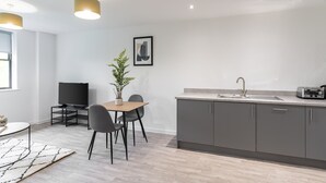 A modern kitchen with grey cabinets, a built-in sink, and a toaster. There is a dining area with a table and chairs, and a potted plant on the table.