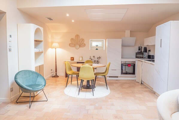 A compact kitchen with a dining area, featuring a round table, chairs, and a built-in oven. - Les Génoises, (Pézenas)