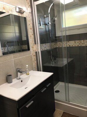 A modern bathroom with a glass-enclosed shower, a white sink, and a mirror above it.