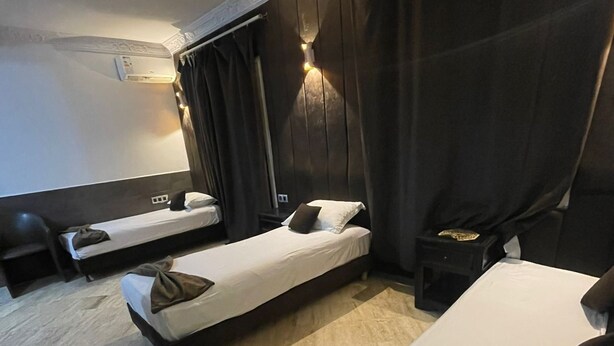 Hotellihuone, jossa on kaksi erillistä sänkyä, sohva, pieni pöytä ja seinälle asennettu ilmastointilaite.