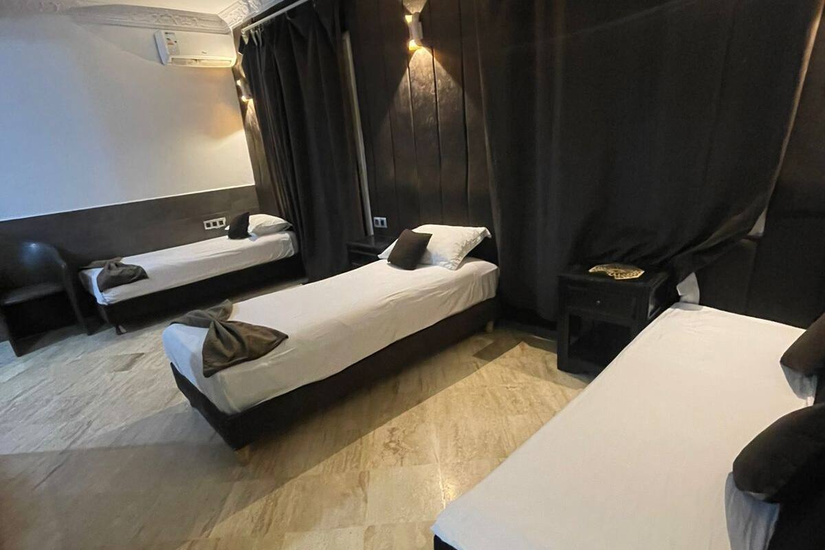 Hotellihuone, jossa on kaksi erillistä sänkyä, sohva, pieni pöytä ja seinälle asennettu ilmastointilaite.