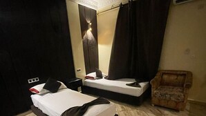 Hotellihuone, jossa on kaksi sänkyä, tuoli, seinään asennettu ilmastointilaite ja koristeellinen valaisin.