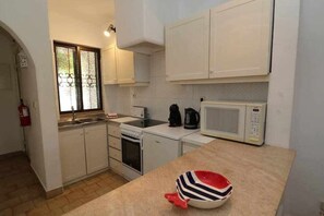 Une cuisine de taille réduite avec des meubles blancs, un four à micro-ondes, une cuisinière et un évier.