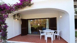A covered patio with a table and chairs, a sliding glass door, and a white wall with purple flowers.