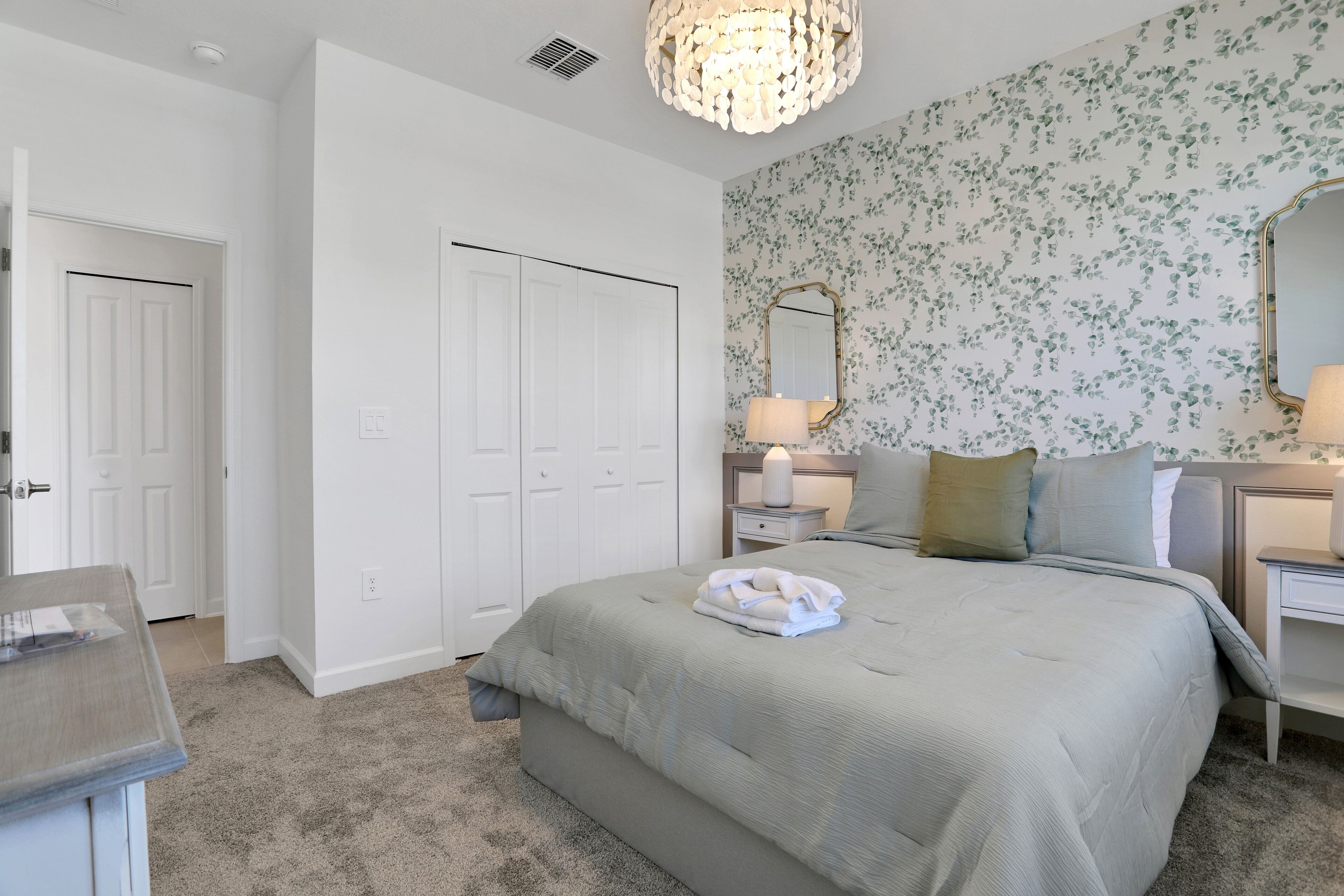 A bedroom with a large bed, two bedside tables, a nightstand, a chandelier, and a floral wallpaper.