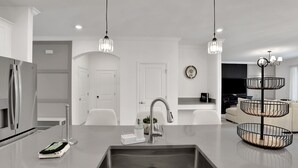 Uma cozinha moderna com pia de aço inoxidável, armários brancos e iluminação pendente.