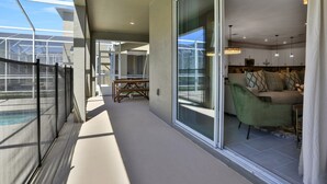 Varanda ampla com piscina, portas de correr para uma sala de estar com sofá e mesa de jantar.