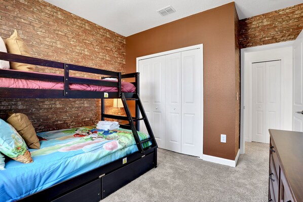 A bunk bed with a blue mattress and pillows, a brick wall, a white door, and a dresser.