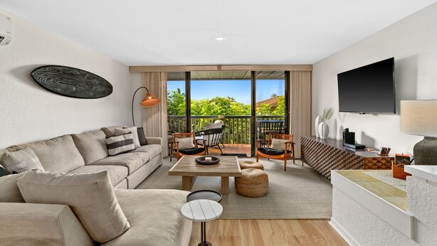 A modern living room with a sofa, coffee table, and chairs, a flat-screen TV, and a balcony with a view of greenery. - Kauai Nihi Kai Villas 507 2 Bedroom Condo (Koloa)