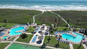 A resort with two swimming pools, sun loungers, umbrellas, and a beach view.