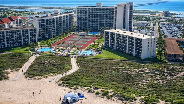 A high-rise hotel with multiple floors, a central courtyard with a tennis court, and a beach area.