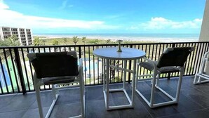 A balcony with a view of the beach and ocean. There are two chairs and a small table.