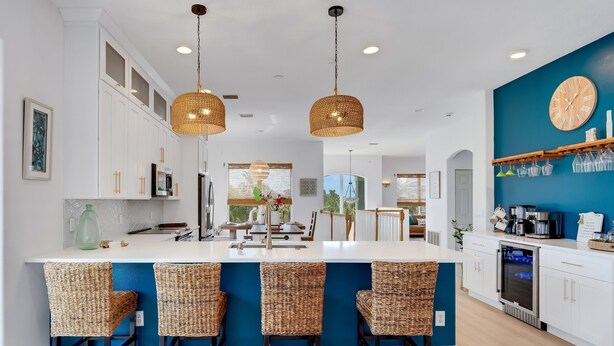 A modern kitchen with white cabinetry, a central island with bar stools, and a blue accent wall.