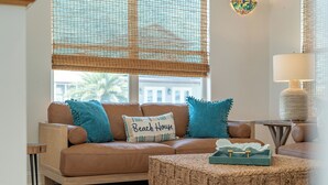 A cozy living room with a brown leather sofa, blue cushions, a woven ottoman, and a lamp on a side table.
