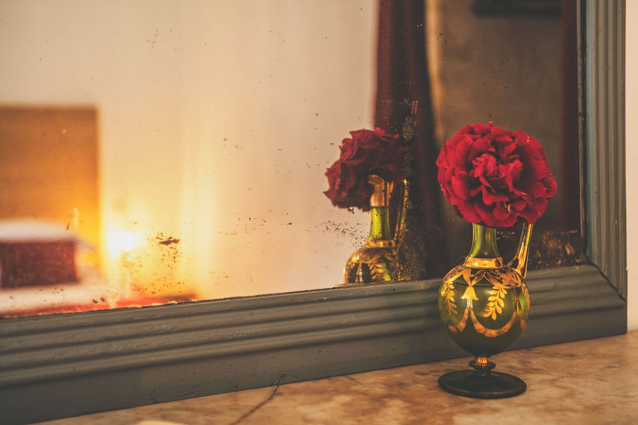 Un miroir reflétant deux vases ornés de fleurs rouges, posés sur une surface en marbre.