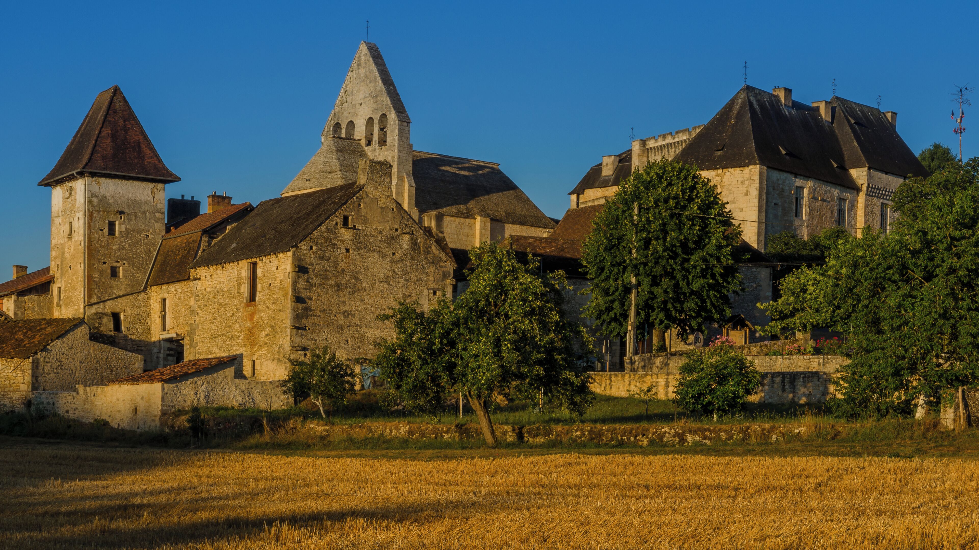 A historic stone building with a prominent tower, surrounded by trees and a field.
