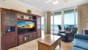 A spacious living room with a large flat-screen TV, a wooden coffee table, a blue sofa, and a leather armchair.