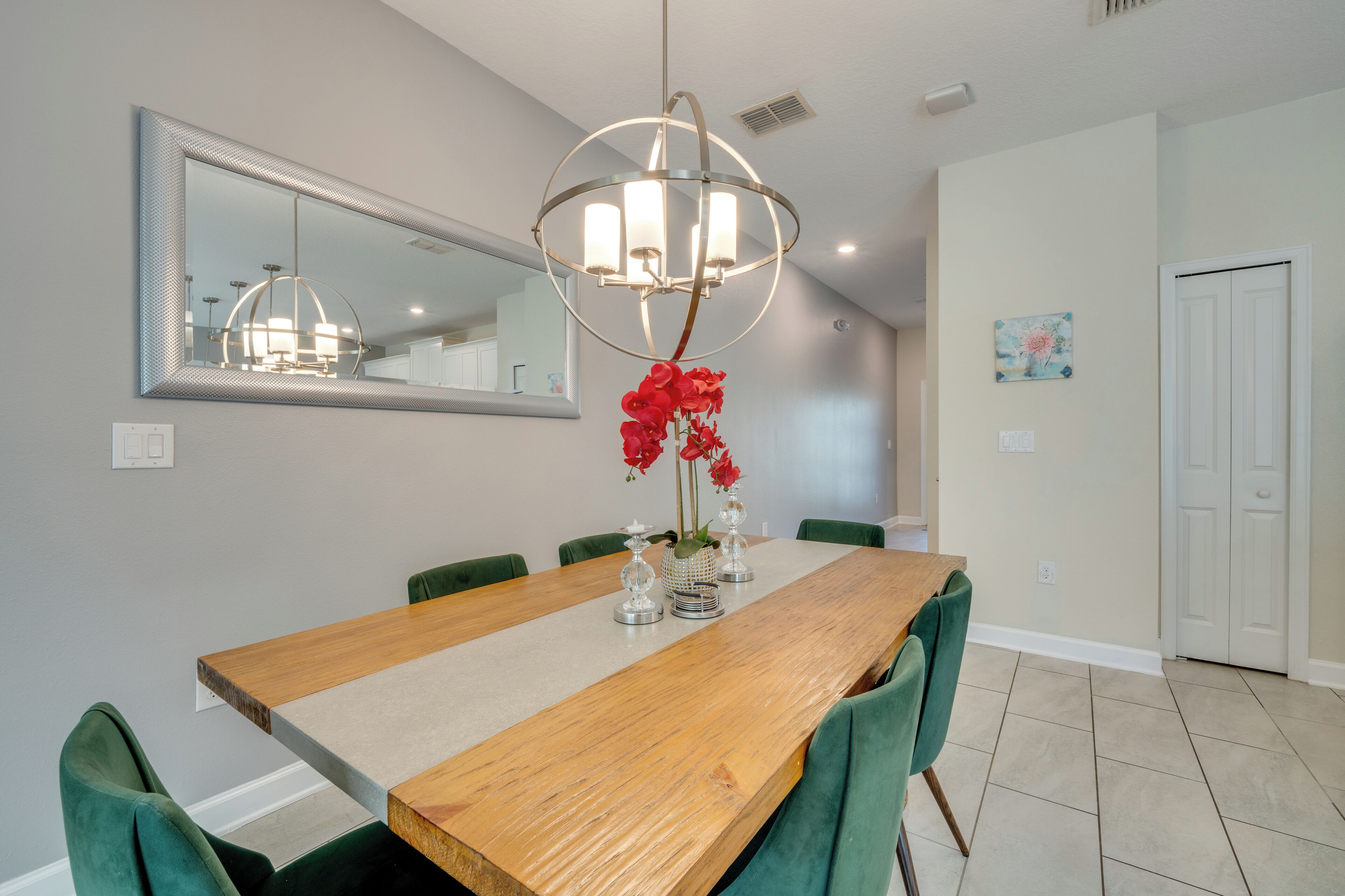 A dining area with a wooden table, green chairs, a chandelier, and a mirror on the wall.