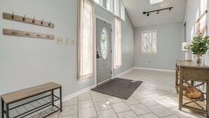 A spacious entryway with a grey door, a bench, a console table with a plant, and a wall-mounted coat rack. - Benton Harbor Home w/ Fire Pit - 2 Mi to Beach! (Benton Harbor)