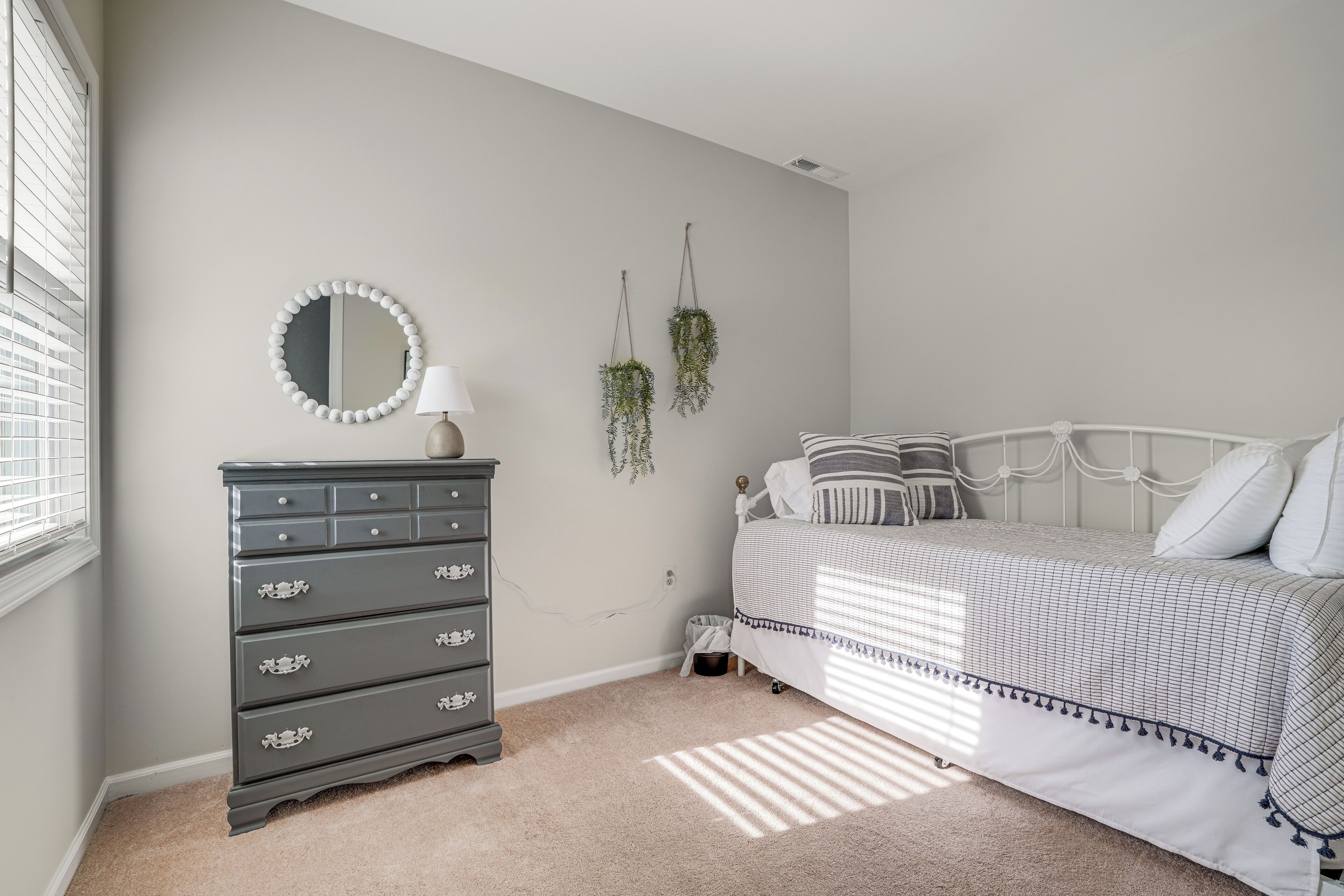 A bedroom with a bed, dresser, mirror, and hanging plants.