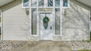 A house with a white exterior, a front door with a decorative wreath, and two wall-mounted light fixtures. - Benton Harbor Home w/ Fire Pit - 2 Mi to Beach! (Benton Harbor)
