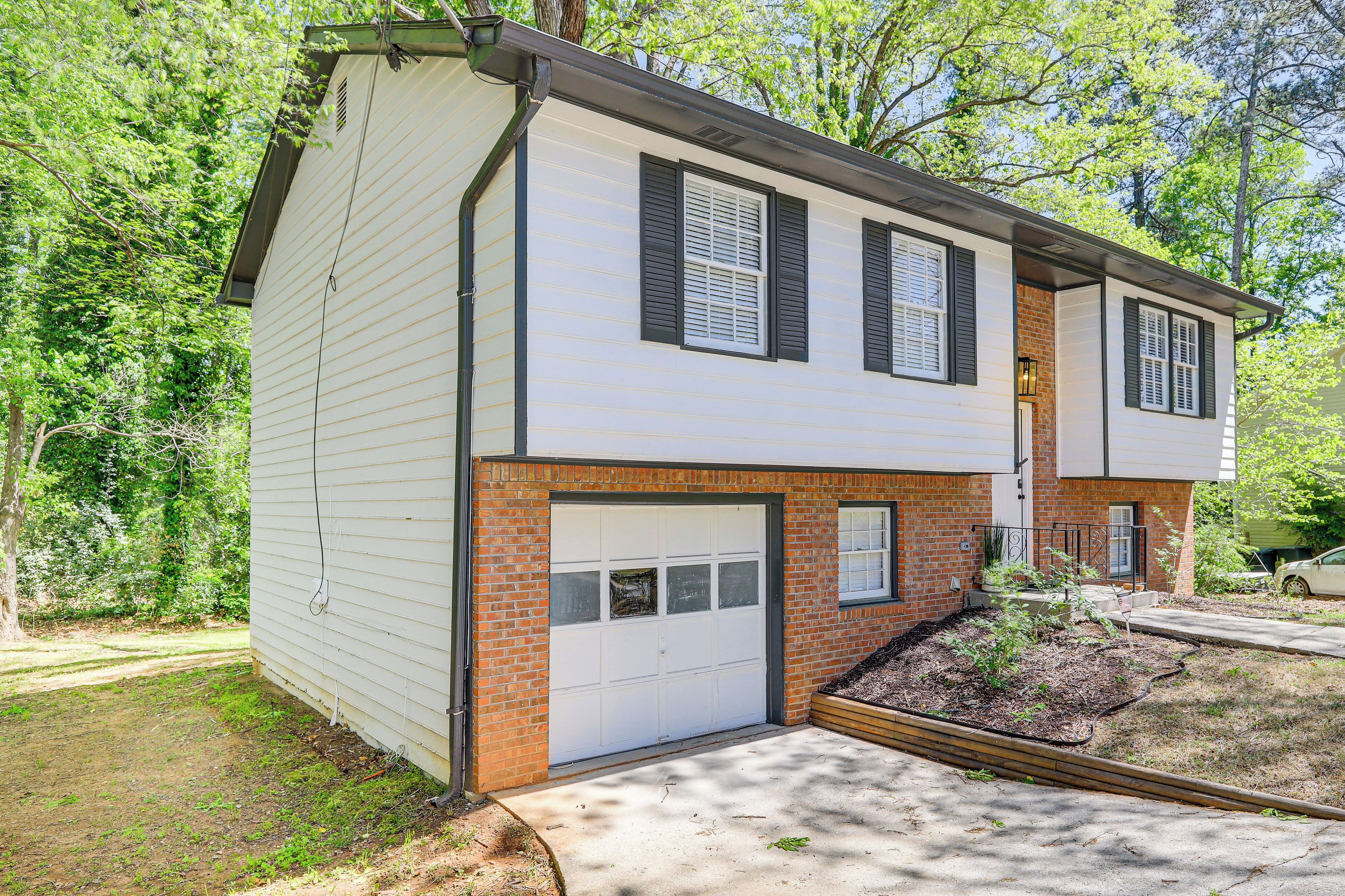A two-story house with a garage, brick foundation, and a small garden area.