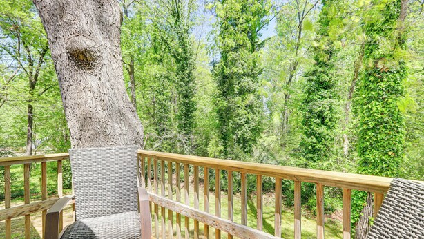 A wooden deck with a wicker chair and a bench, surrounded by trees.