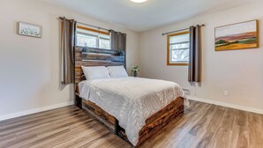 Een slaapkamer met een houten bed, witte lakens en uitzicht op het omliggende landschap door een raam.