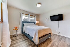 Ein Schlafzimmer mit einem Bett, einem an der Wand montierten Fernseher und einem Fenster mit Vorhängen.