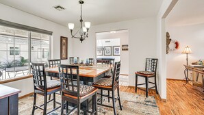 Zona pranzo con tavolo e sedie in legno, un lampadario e vista attraverso ampie finestre.