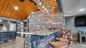 A kitchen with a brick wall, wooden ceiling, and a bar area with stools. - Fire Pit + Dock: Lakefront Cabin in Zimmerman! (Zimmerman)