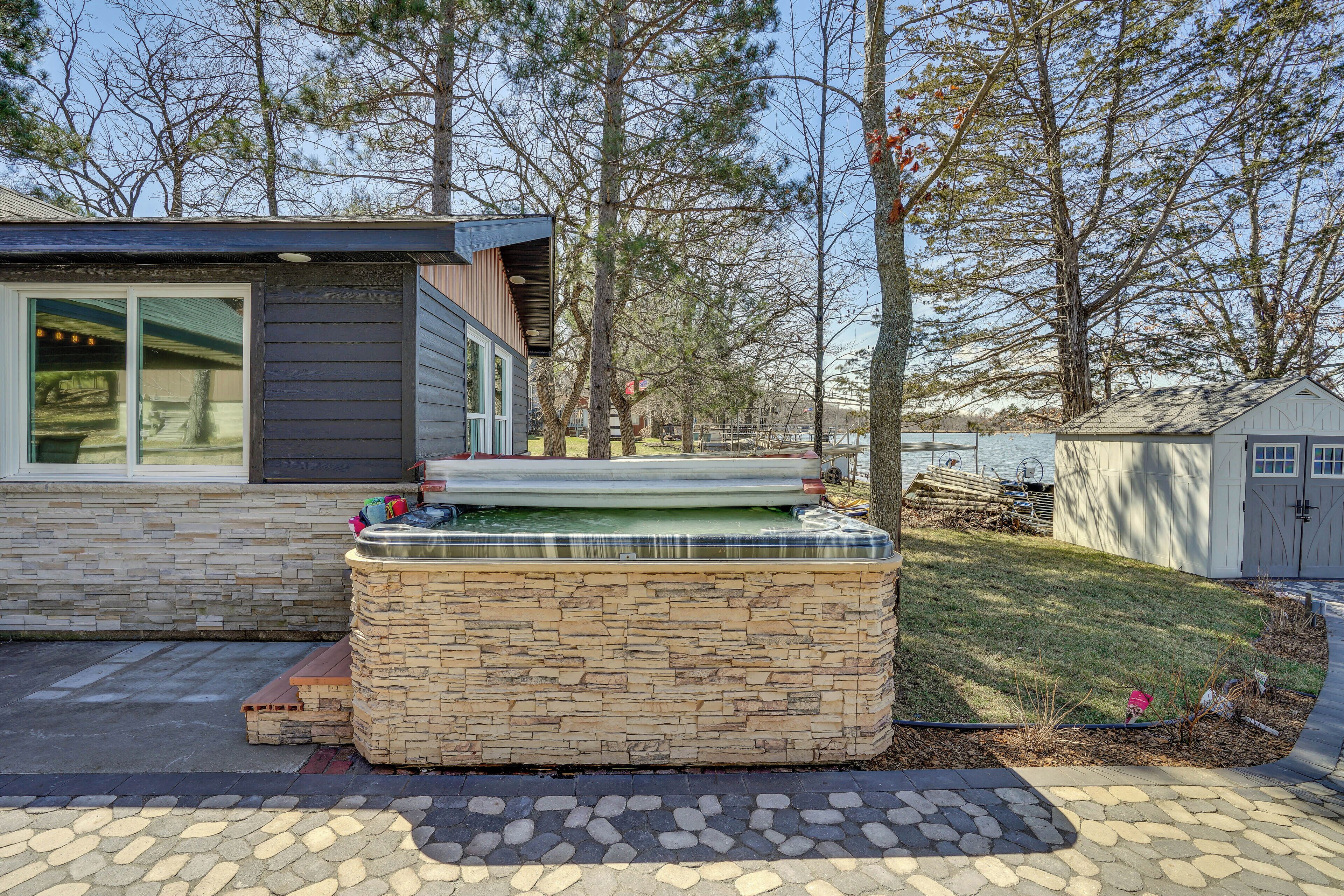 Ein moderner Außenbereich mit Whirlpool, Steinwänden, einer Terrasse und Blick auf ein Haus und Bäume.