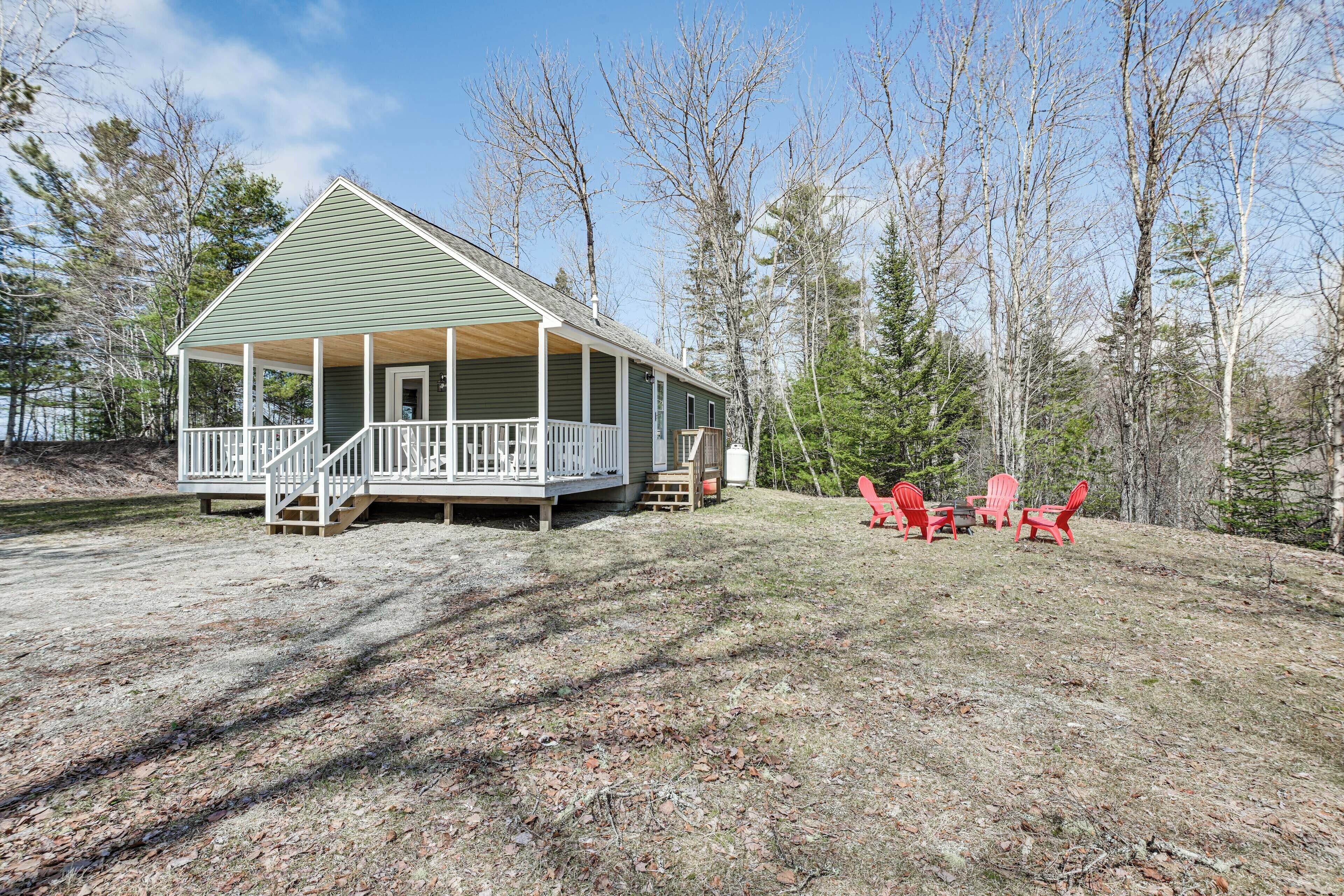 A green house with a porch and a deck, surrounded by trees.