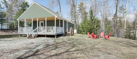 A green house with a porch and a deck, surrounded by trees.