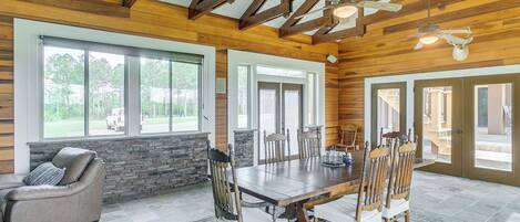 A spacious dining area with a large wooden table and chairs, stone walls, and large windows offering views of the outdoors.