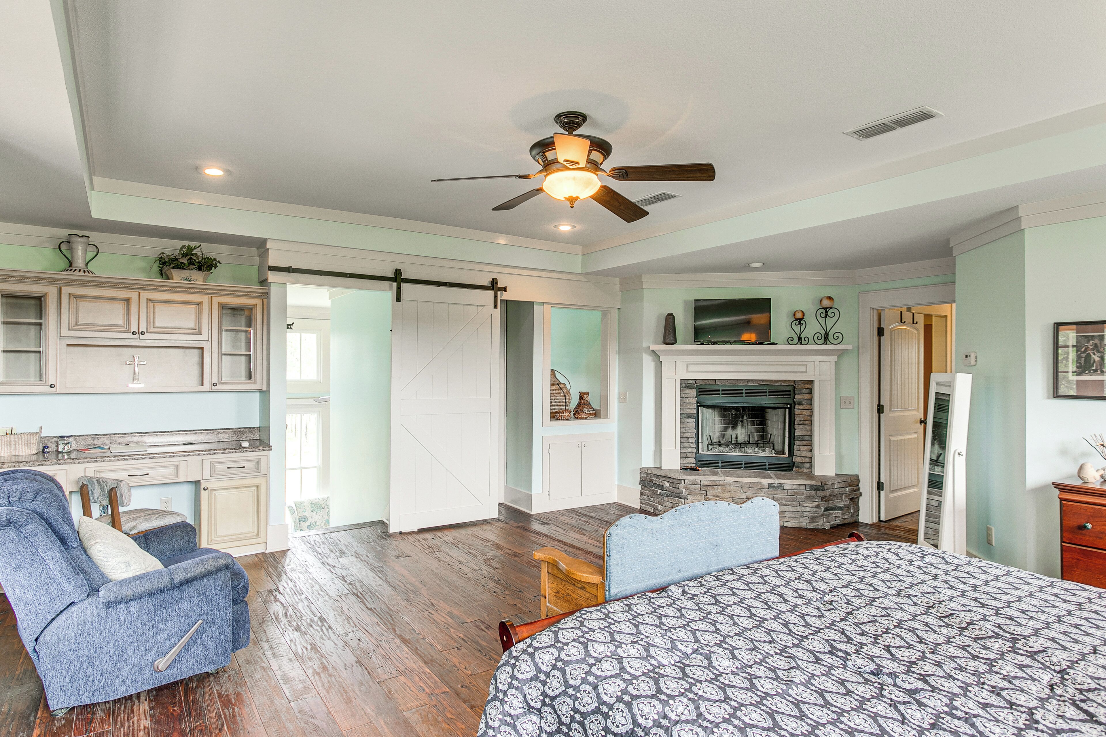A spacious room with a bed, a desk, a chair, a fireplace, and a kitchen area.