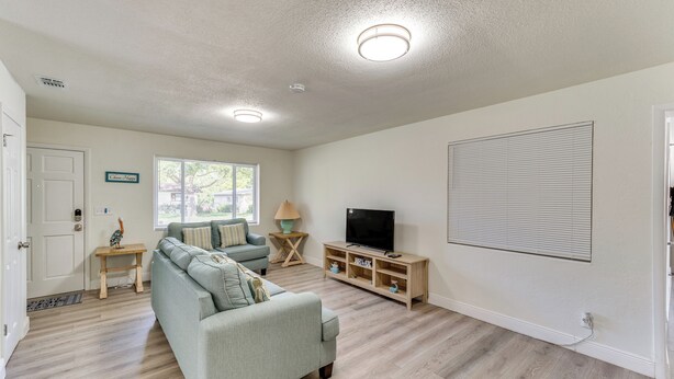 A spacious living room with a light-colored sofa, a television on a wooden stand, and a window with blinds. - Game Room, Private Pool: South Daytona Home! (Daytona Beach)