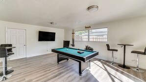 A pool table with surrounding chairs, a television, and a window with blinds. - Game Room, Private Pool: South Daytona Home! (Daytona Beach)
